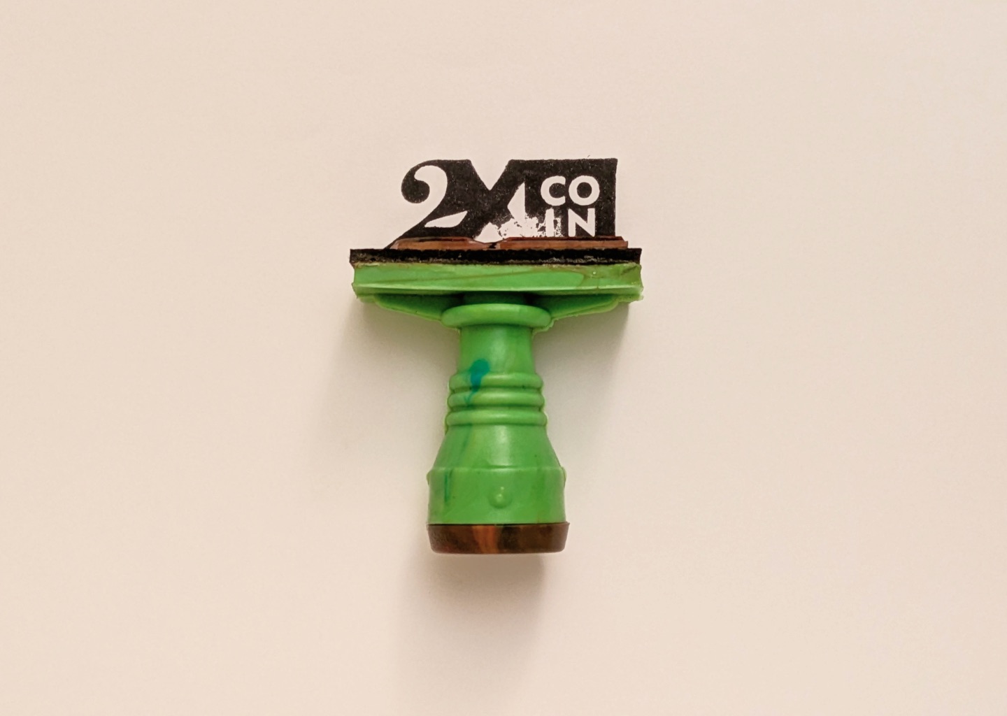Green rubber stamp with the 2XCOIN mark on cream paper