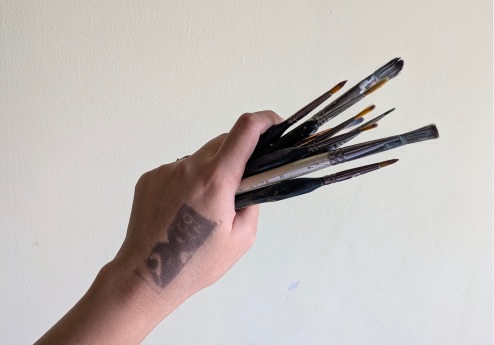 Hand holding paintbrushes with a 2XCOIN stamp on the wrist