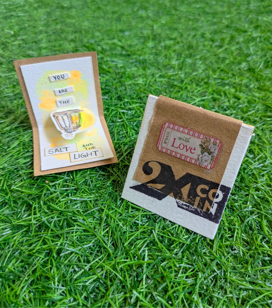 Salt and light card beside a 2XCOIN matchbox on grass
